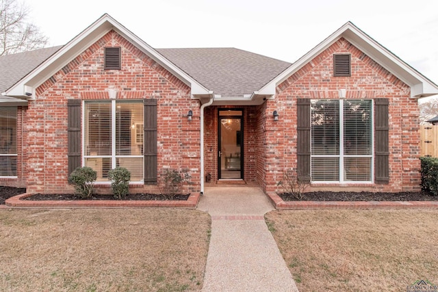 view of front of home featuring roof with shingles, a front yard, and brick siding