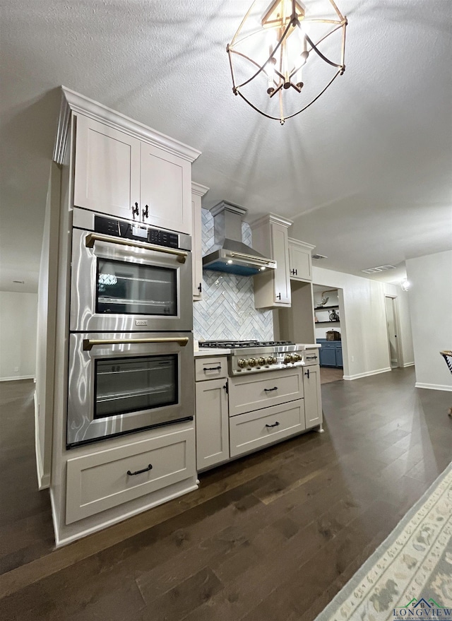 kitchen with appliances with stainless steel finishes, backsplash, dark hardwood / wood-style flooring, wall chimney range hood, and white cabinets