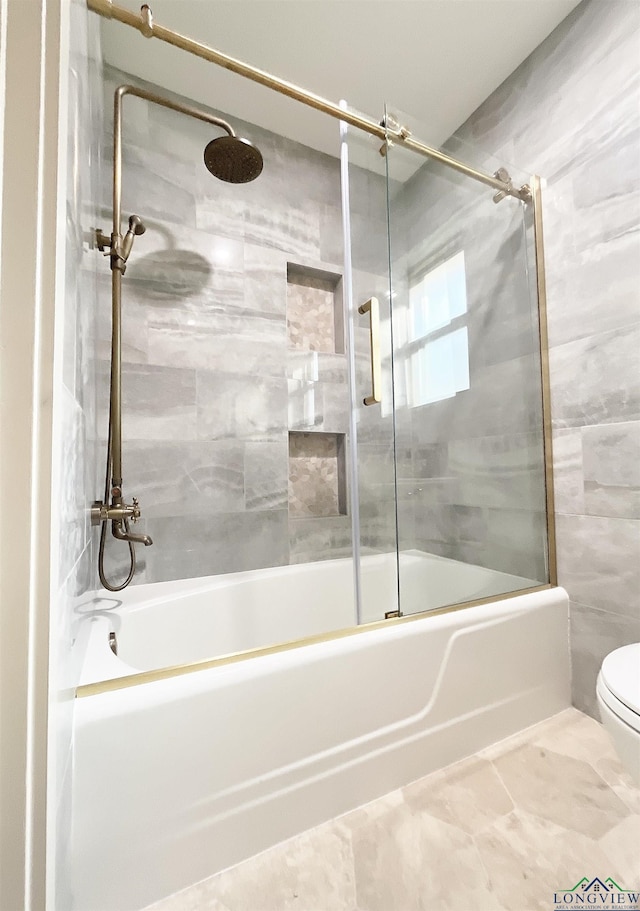 bathroom featuring toilet and shower / bath combination with glass door