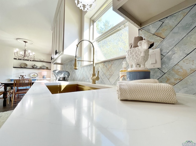 interior details with decorative backsplash, sink, and a chandelier