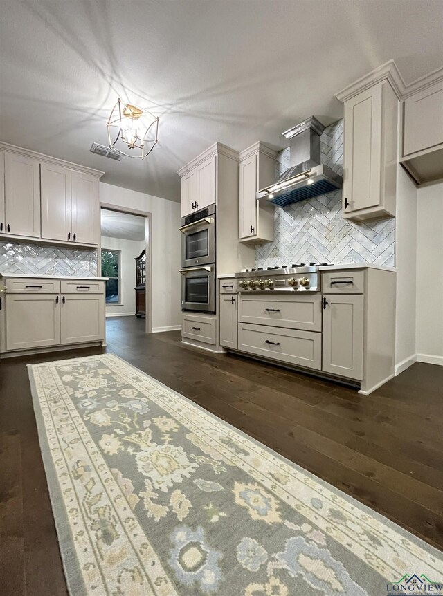 kitchen featuring wall chimney range hood, dark hardwood / wood-style floors, tasteful backsplash, white cabinetry, and stainless steel appliances