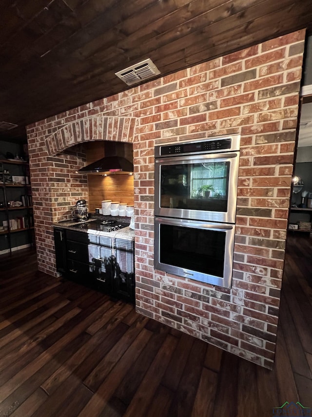 kitchen featuring wooden ceiling, dark wood-type flooring, gas stovetop, range hood, and stainless steel double oven