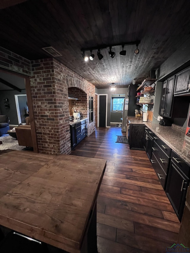 kitchen with light stone countertops, dark hardwood / wood-style flooring, track lighting, and brick wall