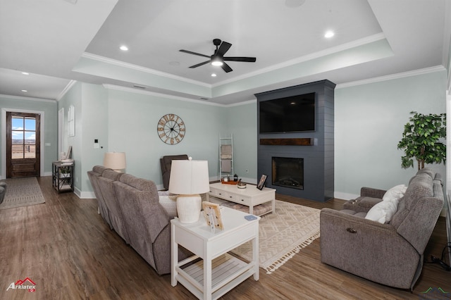 living room with hardwood / wood-style floors, a large fireplace, a tray ceiling, and crown molding