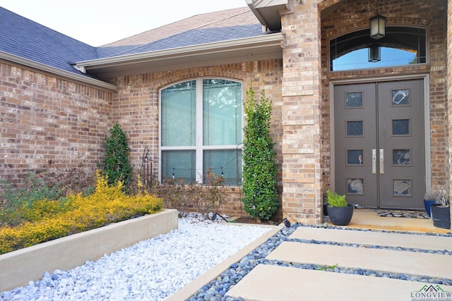 entrance to property featuring brick siding and roof with shingles