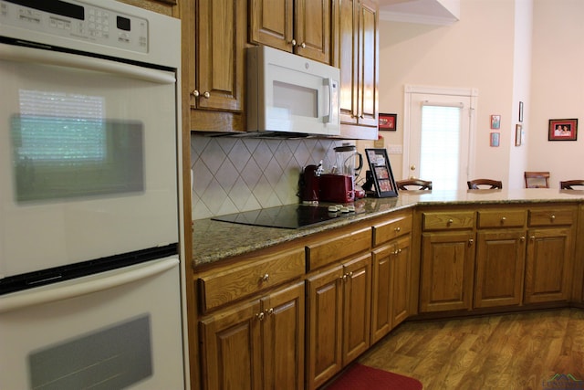 kitchen featuring white appliances, hardwood / wood-style flooring, light stone counters, and tasteful backsplash