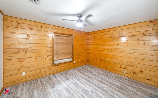 unfurnished room featuring ceiling fan, light hardwood / wood-style flooring, and wood walls