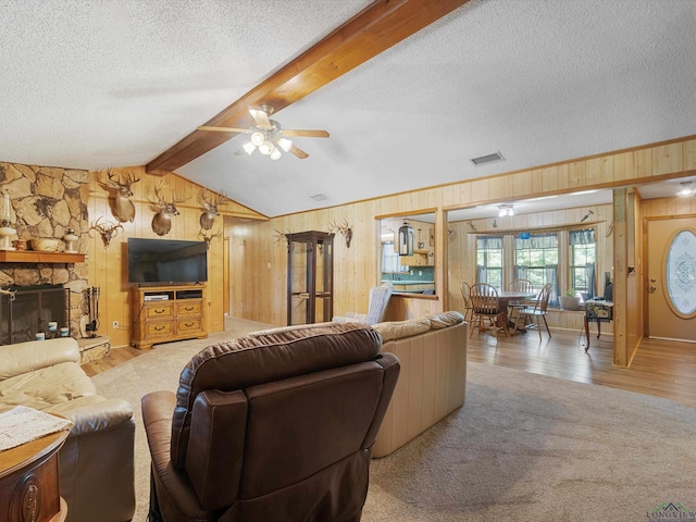 living room with lofted ceiling with beams, a stone fireplace, ceiling fan, a textured ceiling, and light colored carpet