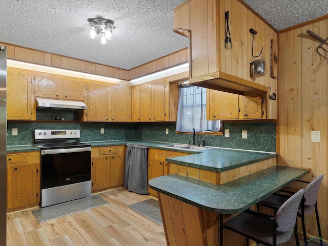 kitchen featuring stainless steel range with electric stovetop, wood walls, sink, light wood-type flooring, and kitchen peninsula