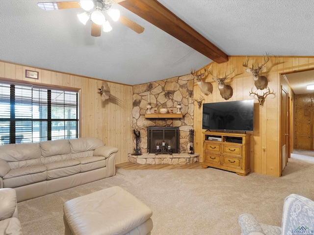 carpeted living room featuring a textured ceiling, a stone fireplace, ceiling fan, and wood walls