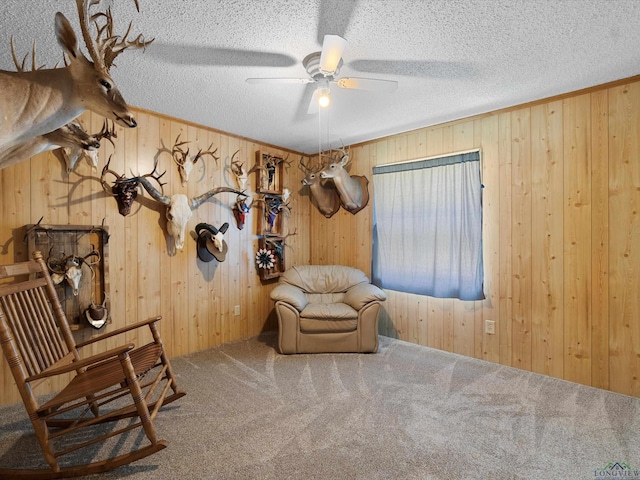 living area with carpet flooring, a textured ceiling, ceiling fan, and wood walls