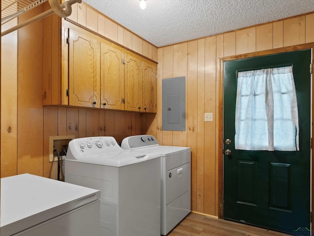 clothes washing area featuring washing machine and clothes dryer, cabinets, electric panel, wood walls, and a textured ceiling