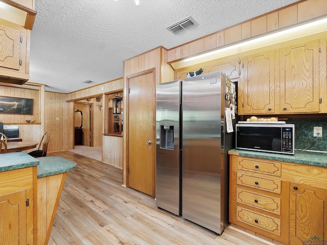 kitchen with a textured ceiling, wood walls, light hardwood / wood-style flooring, and stainless steel refrigerator with ice dispenser