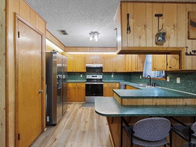 kitchen featuring kitchen peninsula, appliances with stainless steel finishes, a breakfast bar, sink, and light hardwood / wood-style flooring