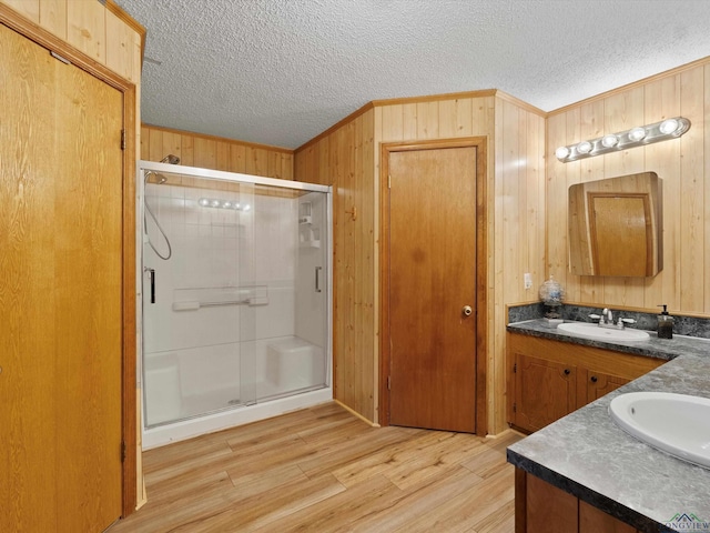 bathroom featuring hardwood / wood-style floors, a textured ceiling, wooden walls, vanity, and a shower with shower door