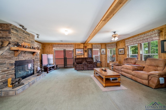 living room featuring beamed ceiling, carpet floors, a stone fireplace, and wooden walls