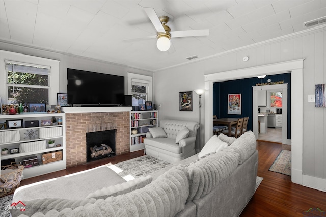 living room with a brick fireplace, visible vents, dark wood finished floors, and crown molding