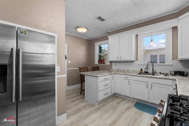 kitchen with visible vents, appliances with stainless steel finishes, white cabinetry, a sink, and a peninsula