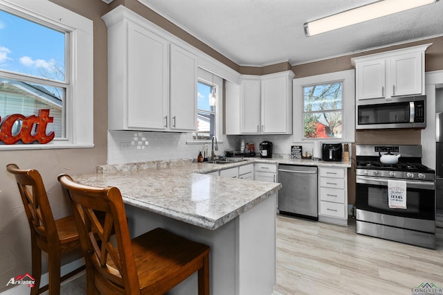 kitchen featuring a breakfast bar area, stainless steel appliances, a peninsula, a sink, and white cabinetry