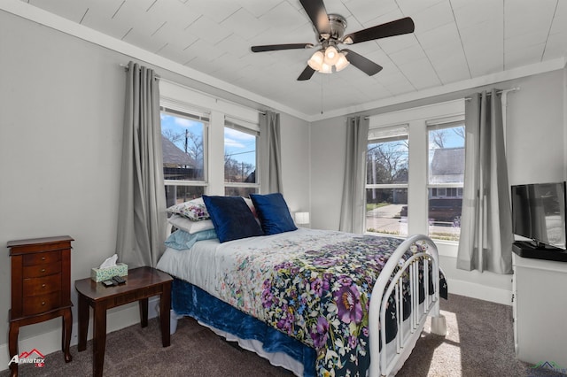 bedroom featuring dark colored carpet, ornamental molding, multiple windows, and a ceiling fan