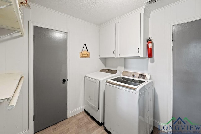 laundry room with cabinets, ornamental molding, light wood-type flooring, a textured ceiling, and washing machine and clothes dryer