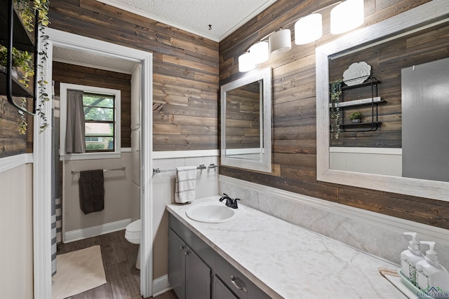 bathroom with hardwood / wood-style floors, vanity, wooden walls, toilet, and a textured ceiling