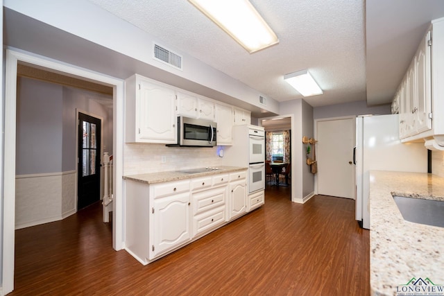 kitchen with light stone countertops, a textured ceiling, white appliances, and white cabinetry