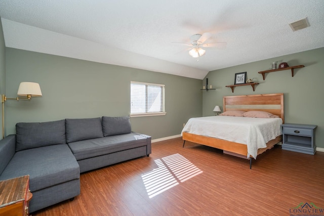 bedroom with a textured ceiling, hardwood / wood-style flooring, vaulted ceiling, and ceiling fan