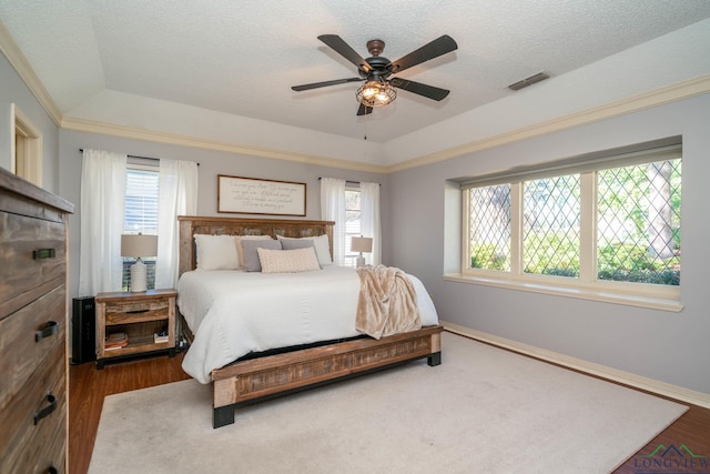 bedroom featuring ceiling fan, wood-type flooring, a textured ceiling, and a tray ceiling