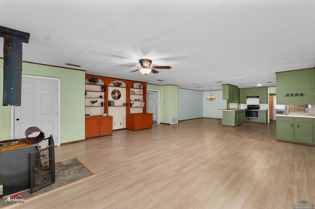 unfurnished living room with wood walls, ceiling fan, light hardwood / wood-style floors, and sink