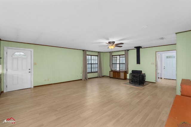 unfurnished living room with a wood stove, ceiling fan, and light hardwood / wood-style flooring