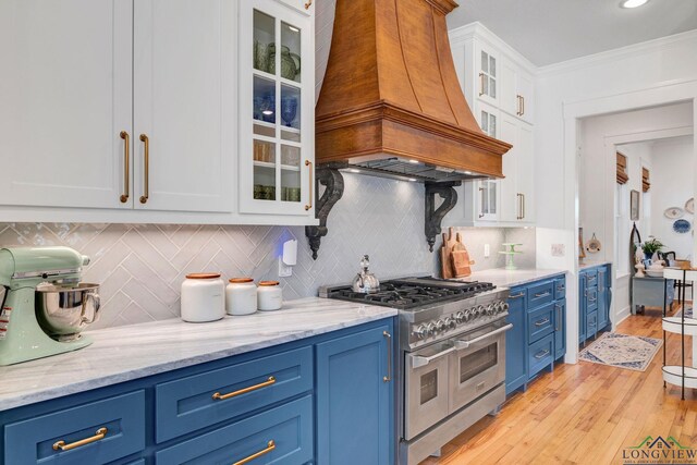 kitchen featuring custom exhaust hood, light stone countertops, range with two ovens, white cabinetry, and backsplash