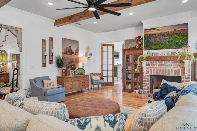 living room with hardwood / wood-style flooring, a brick fireplace, beam ceiling, ornamental molding, and ceiling fan