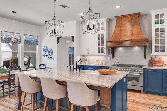 kitchen featuring blue cabinetry, an island with sink, high end stainless steel range, and custom range hood