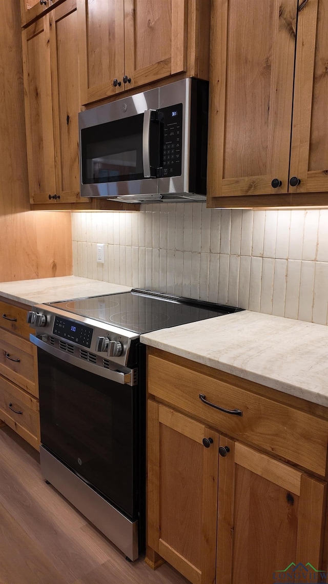 kitchen featuring stainless steel appliances, brown cabinetry, light wood-style floors, and decorative backsplash