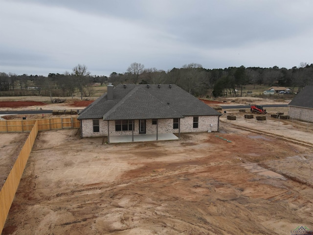 view of front of house featuring a patio, a shingled roof, a chimney, and fence