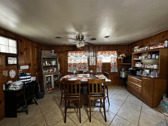 dining area featuring wooden walls, a textured ceiling, a ceiling fan, and light tile patterned flooring