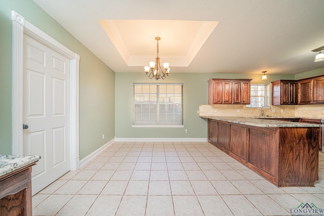 kitchen featuring light stone counters, backsplash, a tray ceiling, and kitchen peninsula