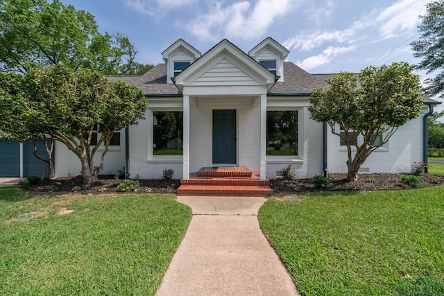 view of front of home featuring roof with shingles, a front yard, and brick siding