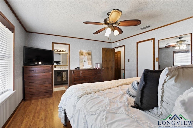 bedroom featuring light wood-type flooring, visible vents, crown molding, and a textured ceiling