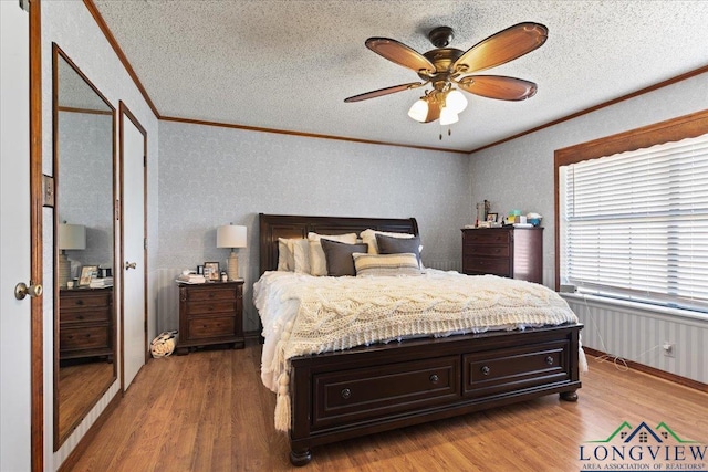 bedroom featuring light wood finished floors, ceiling fan, ornamental molding, and a textured ceiling