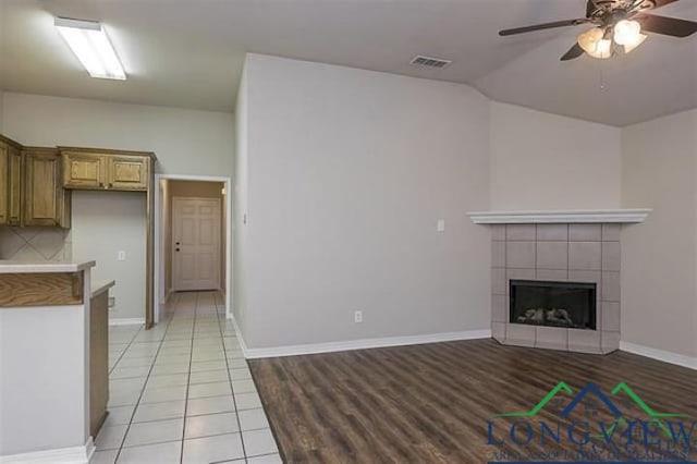 unfurnished living room with light wood-style flooring, a tiled fireplace, visible vents, lofted ceiling, and ceiling fan