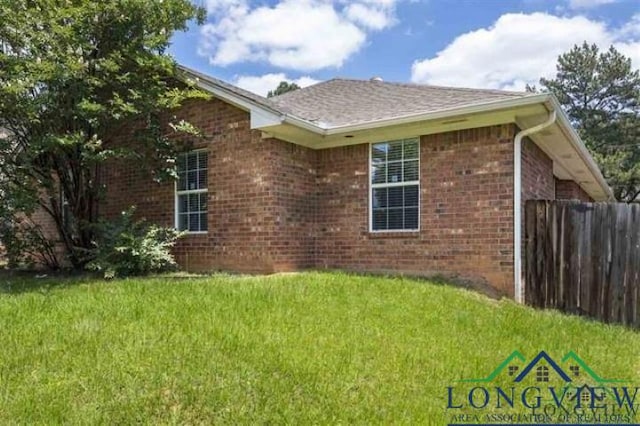 view of side of home featuring fence, a lawn, and brick siding