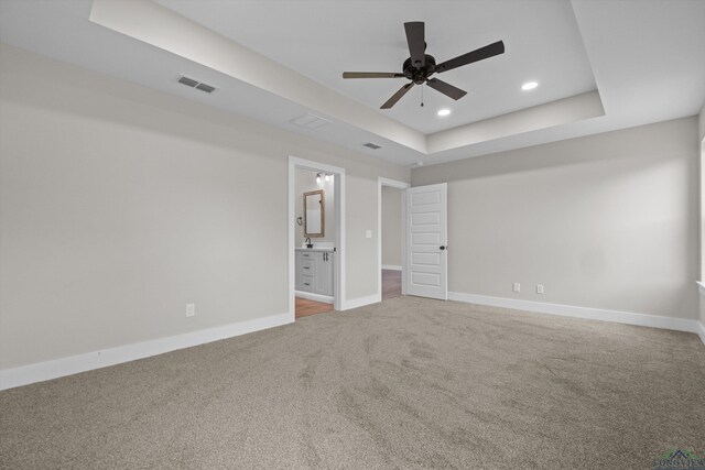 unfurnished bedroom featuring ceiling fan, carpet, a tray ceiling, and ensuite bathroom