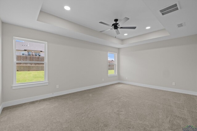 empty room featuring ceiling fan, a raised ceiling, and carpet flooring