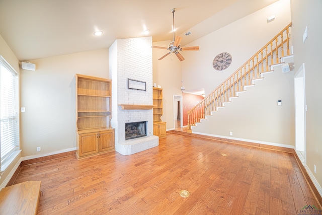 unfurnished living room with ceiling fan, light hardwood / wood-style floors, high vaulted ceiling, and a brick fireplace