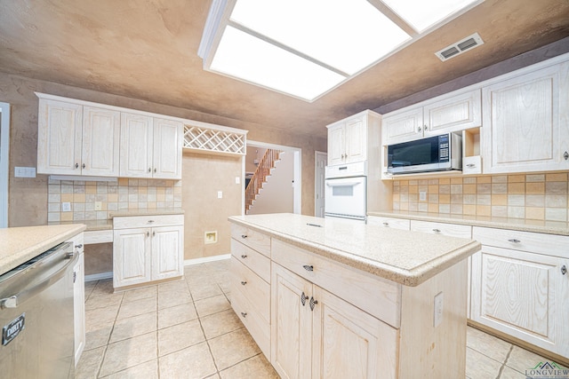 kitchen featuring light stone countertops, stainless steel appliances, a kitchen island, decorative backsplash, and light tile patterned flooring