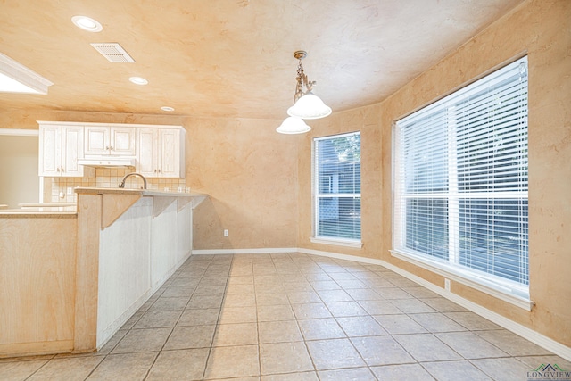 kitchen featuring decorative light fixtures, light tile patterned flooring, kitchen peninsula, and backsplash