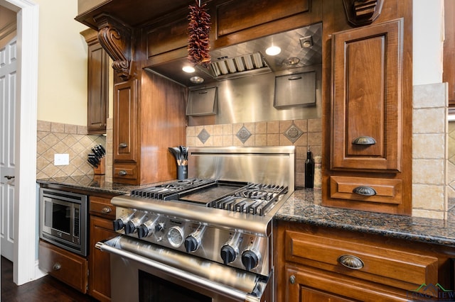 kitchen with dark stone counters, dark wood finished floors, brown cabinetry, stainless steel appliances, and decorative backsplash