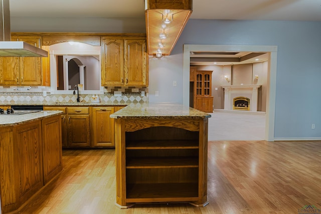 kitchen featuring light stone countertops, tasteful backsplash, sink, a center island, and light hardwood / wood-style floors